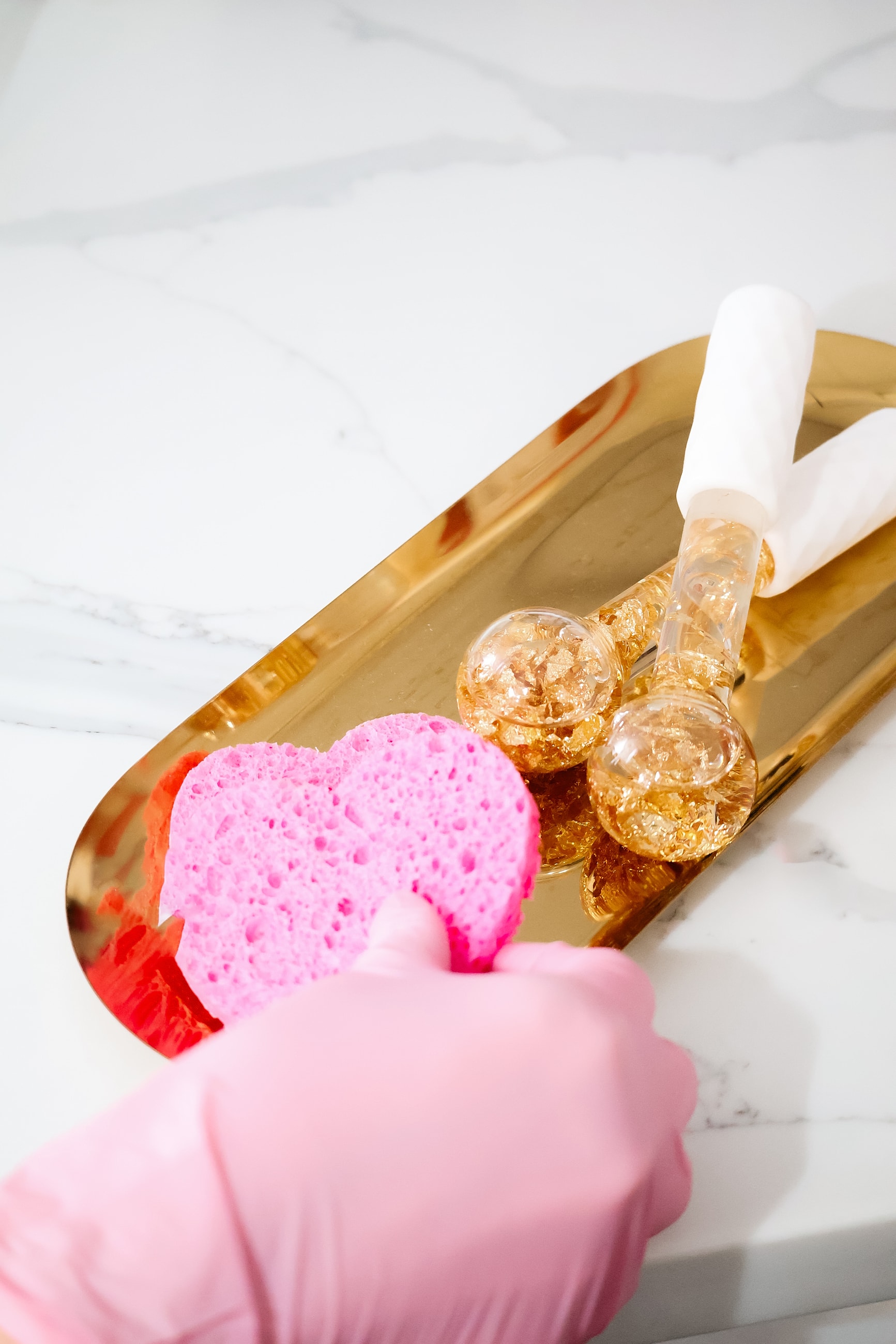 Pink sponge and glass tools on gold tray.