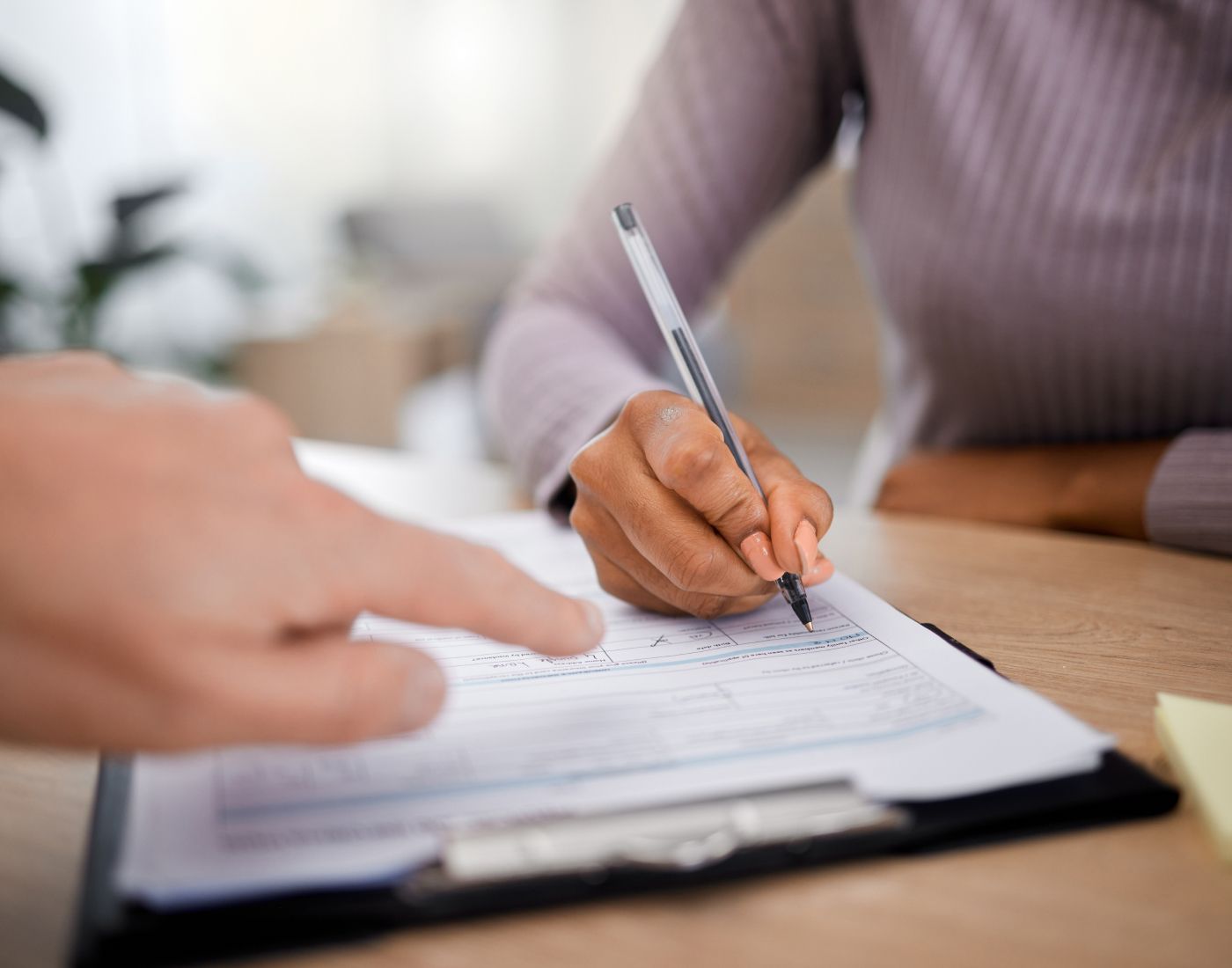 Person signing document with guidance from another.